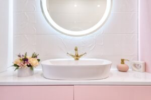 Interior of modern bathroom with luminous mirror hanging under sink with faucet near blooming flowers and soap